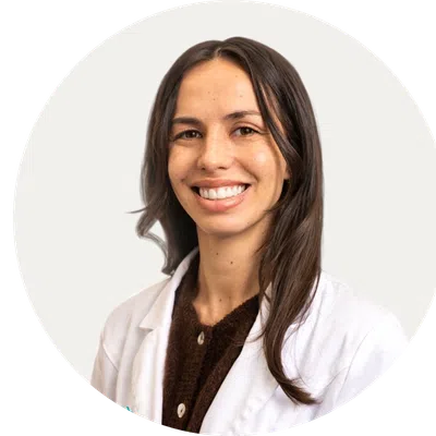 Smiling woman with long brown hair wearing a white lab coat and brown sweater on white background