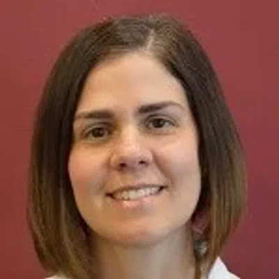 Portrait of a smiling woman with straight brown hair against a solid red background.