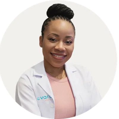 Smiling female healthcare professional wearing a white lab coat and pink top with braided hair in a bun.