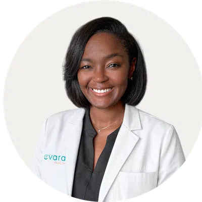 Professional smiling female healthcare worker wearing a white coat with Evara Health logo on it