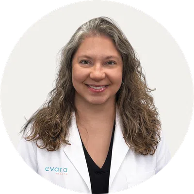 Smiling female healthcare professional with long curly hair wearing a white Evara Health lab coat