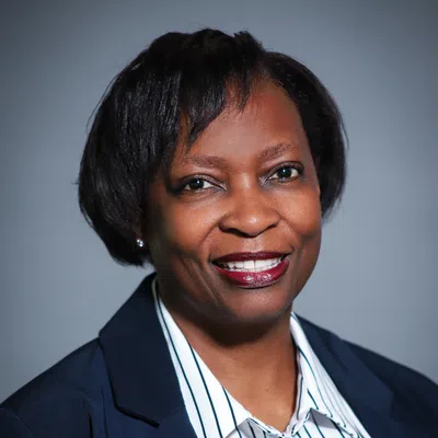 Professional smiling Black woman in a navy blazer and striped white shirt against a plain background