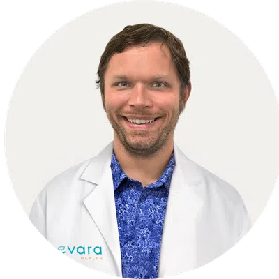 Smiling male healthcare professional wearing a white coat over a blue patterned shirt in a circular frame