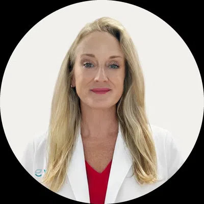 Portrait of a confident female doctor with long blonde hair wearing a white coat and red blouse.