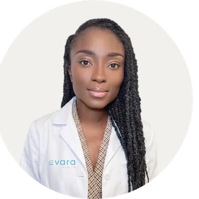 Portrait of a confident Black female doctor wearing a white coat with Evara Health logo on white background.