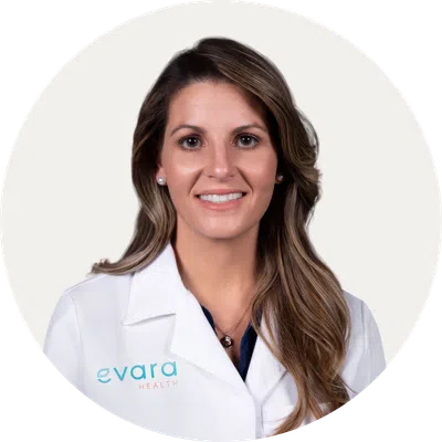Smiling female healthcare professional with long hair wearing a white lab coat with Evara Health logo