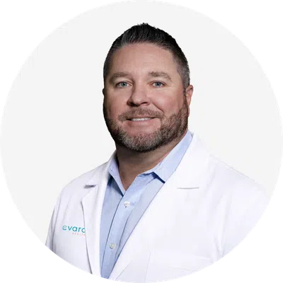 Smiling male doctor wearing a white lab coat and light blue shirt on a white background.