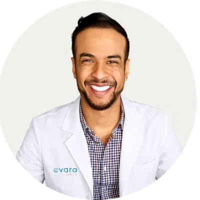 Smiling male doctor wearing a white lab coat over black scrubs against a white background