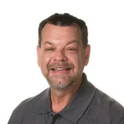 Smiling middle-aged man with short hair and beard wearing a dark gray polo shirt against white background