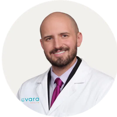 Smiling male doctor wearing a white lab coat and purple tie against a light background
