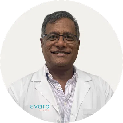 Smiling male doctor wearing glasses and white lab coat with Evara Health logo on left side.