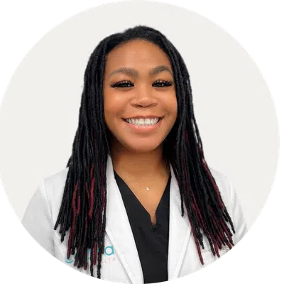 Smiling healthcare professional with red dreadlocks wearing a white Evara Health lab coat against white background