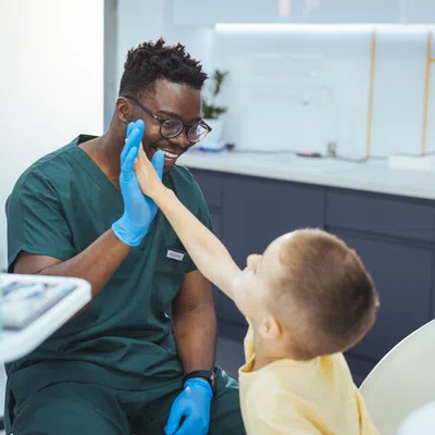 Smiling dentist giving high five to young boy in dental clinic chair during appointment