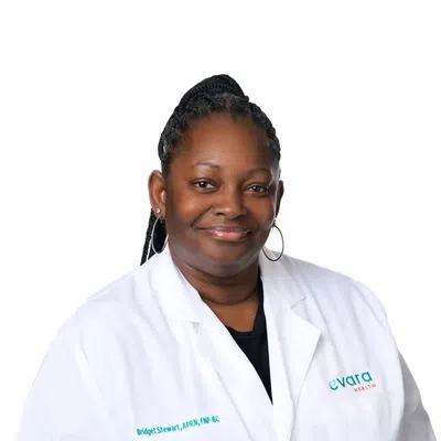 Smiling female healthcare professional in white coat with name and Evara Health logo on a white background.
