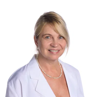 Smiling female healthcare professional in white coat with Evara Health logo and pearl necklace on white background
