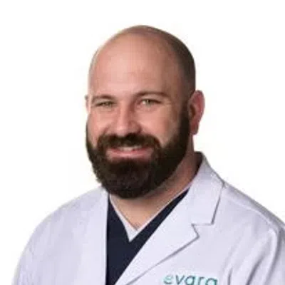 Smiling male healthcare professional in a white lab coat with Evara Health logo on chest.