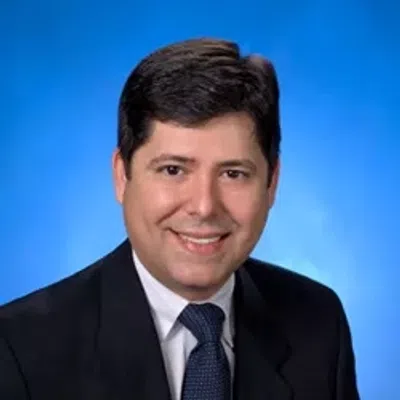 Professional man in dark suit and tie smiling against a blue studio background