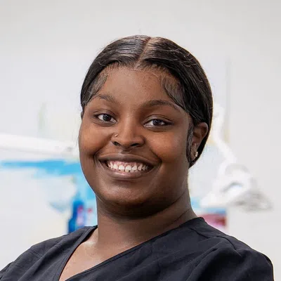 Smiling young woman with nose piercing wearing black medical scrubs in a bright clinical setting.