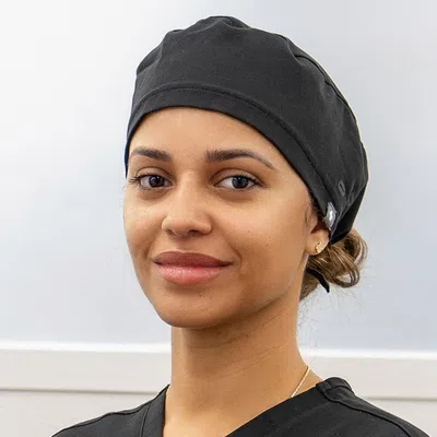 Smiling female healthcare worker wearing black scrubs and a black scrub cap in a clinical setting