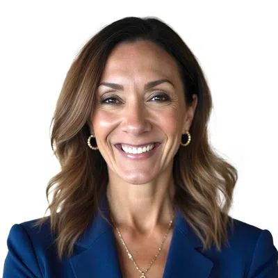 Smiling woman with wavy brown hair wearing a blue blazer, gold hoop earrings, and a pendant necklace.