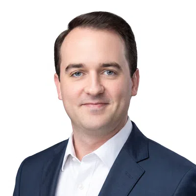 Portrait of a smiling man with blue eyes and dark hair wearing a suit and white shirt on a white background