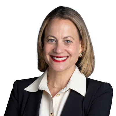 Professional woman in black blazer and white blouse smiling with arms crossed against white background.