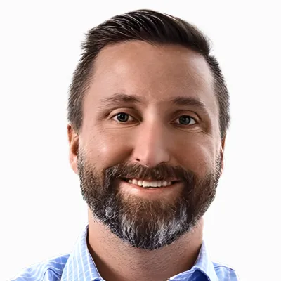 Smiling man with dark hair and beard wearing a light blue checkered shirt on white background