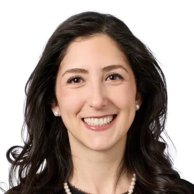 Smiling woman with short curly dark hair wearing a purple beaded necklace against a white background