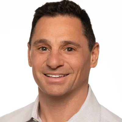 Smiling man with glasses wearing a navy suit and light blue shirt on white background
