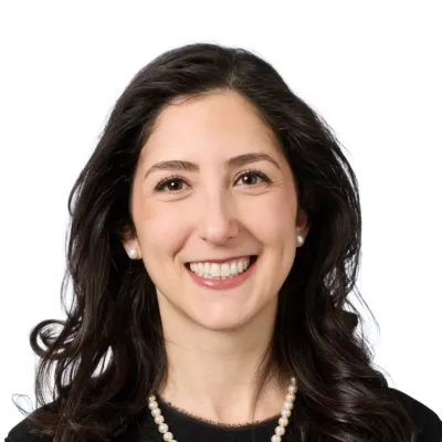Smiling woman with short curly dark hair wearing a purple beaded necklace against a white background