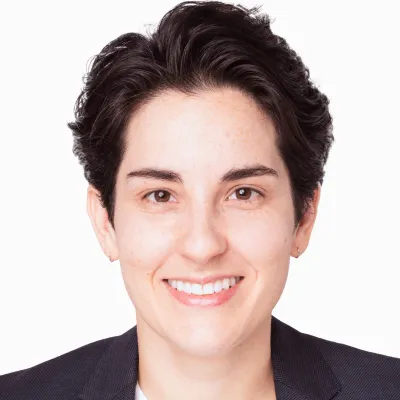 Smiling person with short dark hair wearing a dark blazer against a white background.