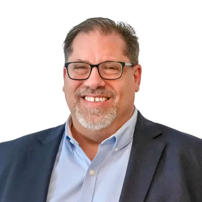 Middle-aged man with salt-and-pepper beard wearing a navy blue blazer and white shirt smiling at the camera