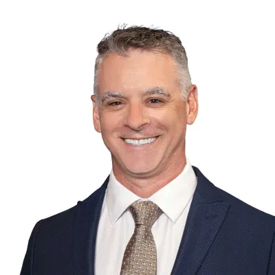 Smiling middle-aged man in navy suit and patterned beige tie against white background