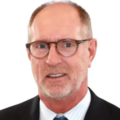 Middle-aged man with glasses wearing a suit, white shirt, and patterned blue tie, smiling slightly against white background.
