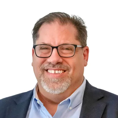 Middle-aged man with salt-and-pepper beard wearing a navy blue blazer and white shirt smiling at the camera