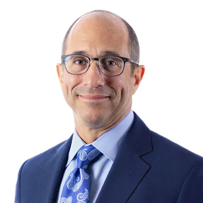 Professional middle-aged man with glasses wearing blue suit and patterned tie against white background