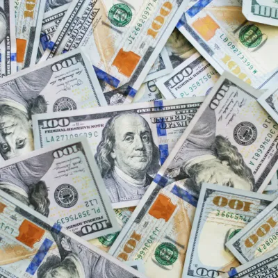 Scattered U.S. one hundred dollar bills featuring Benjamin Franklin's portrait and security features.