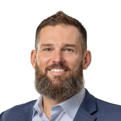 Smiling bearded man in a blue checkered blazer and patterned shirt on a white background