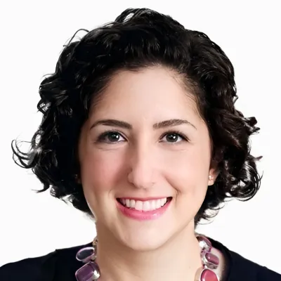 Smiling woman with short curly dark hair wearing a purple beaded necklace against a white background