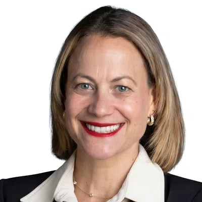 Professional woman in black blazer and white blouse smiling with arms crossed against white background.