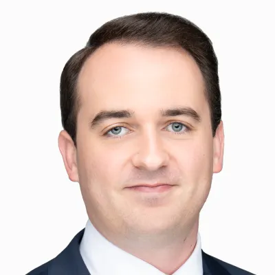 Portrait of a smiling man with blue eyes and dark hair wearing a suit and white shirt on a white background