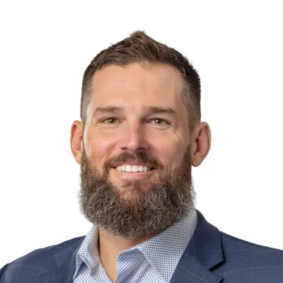 Smiling bearded man in a blue checkered blazer and patterned shirt on a white background