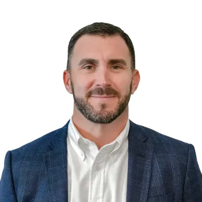 Professional man with short dark hair wearing a suit, light blue shirt, and patterned tie against white background