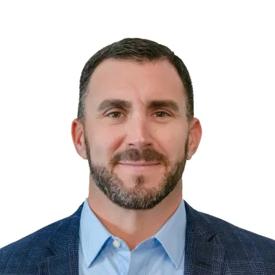 Professional man with short dark hair wearing a suit, light blue shirt, and patterned tie against white background