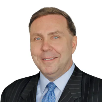 Smiling man in pinstripe suit with blue patterned tie and light blue shirt against white background
