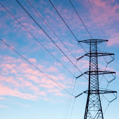 High voltage power transmission tower against a blue sky with soft pink clouds during sunset.