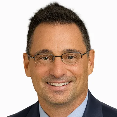 Smiling man with glasses wearing a navy suit and light blue shirt on white background