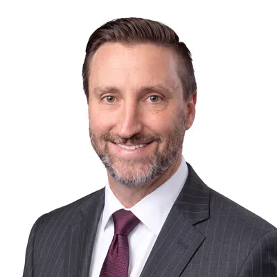 Smiling man in a dark pinstripe suit and maroon tie with neatly styled hair and beard on a gray background