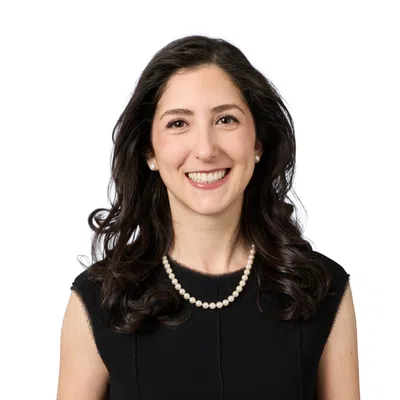 Smiling woman with short curly dark hair wearing a purple beaded necklace against a white background
