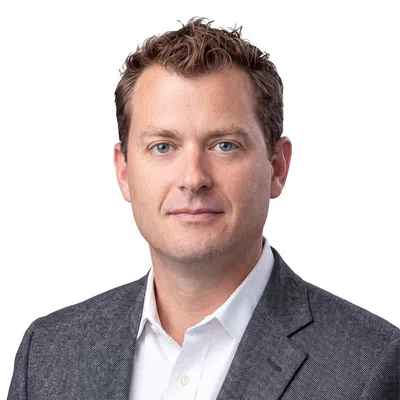Professional headshot of a man with blue eyes wearing a white shirt and gray blazer on white background